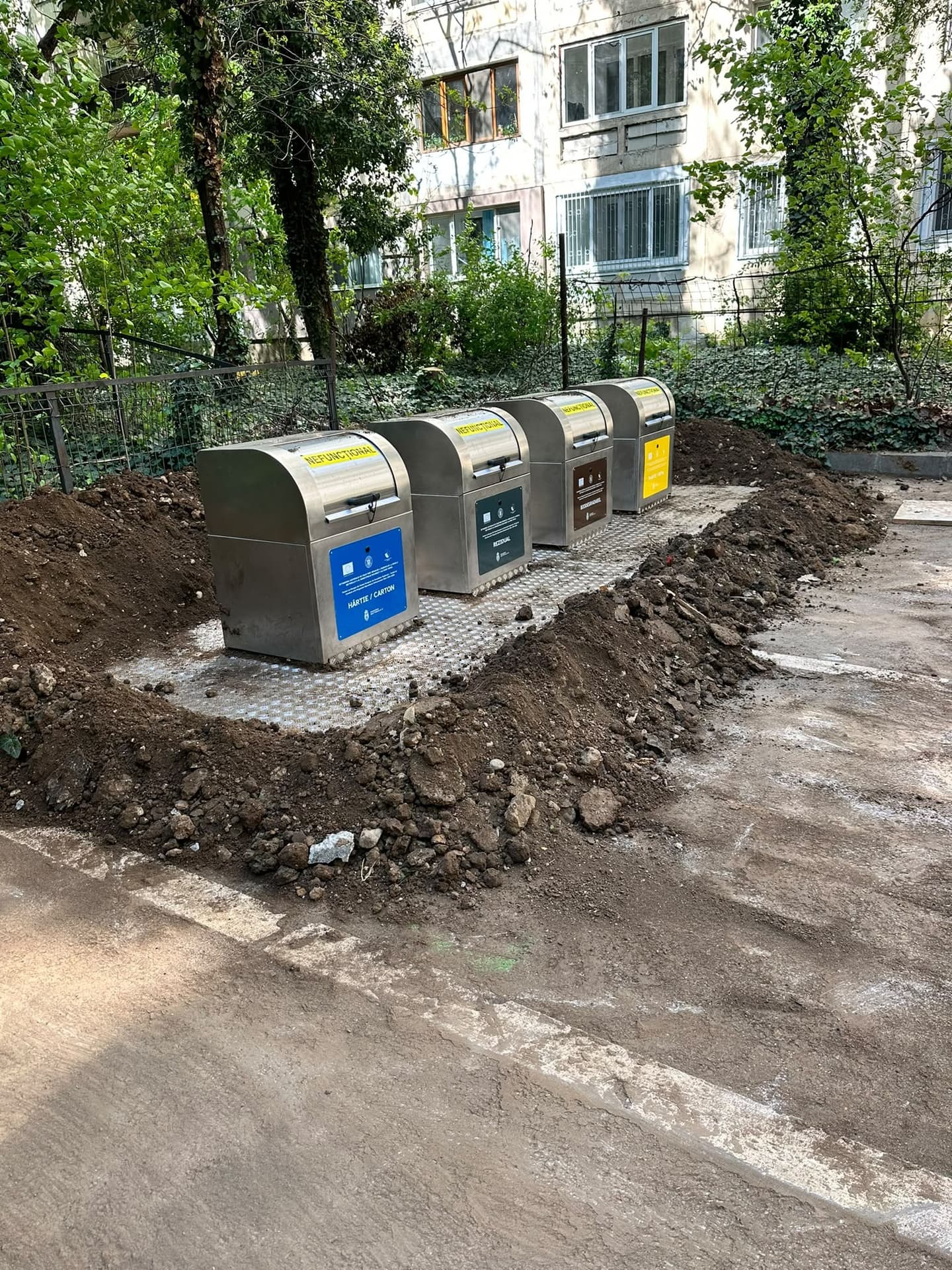Patru containere de gunoi semi-îngropate din inox, pentru colectare selectivă, montate în curtea unui bloc