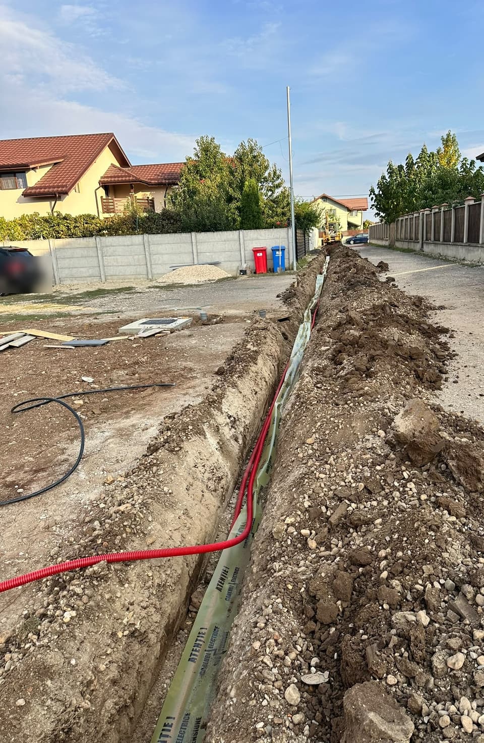 Șanț cu tuburi corugate roșii și bandă galbenă de avertizare pentru cabluri electrice sub tensiune