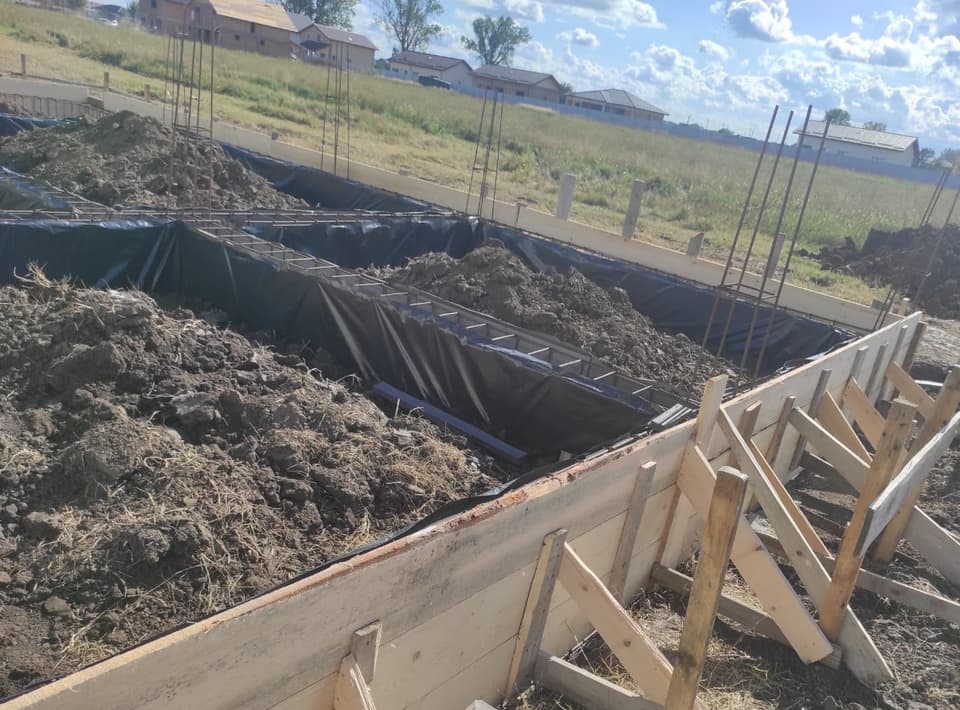 Tranșee pentru fundația unei case, cu armătură montată și pământ excavat depus alături